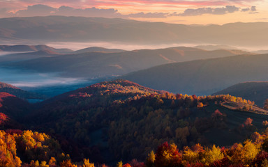 Naklejka na ściany i meble gorgeous red sunrise in mountains. forested hills in colorful fall foliage. fog in the distant valley