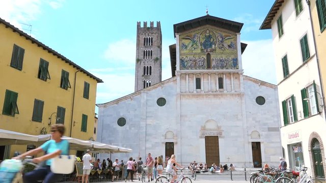 Sightseeing bike tour of Italian landmarks, tourists travel to Tuscany. People walking and taking picture in front of San Frediano church, Lucca, ancient monument of Europe