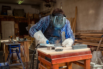 A young  man welder in  uniform, welding mask and welders leathers, weld  metal  with a arc welding machine in workshop, blue and orange  sparks fly to the sides