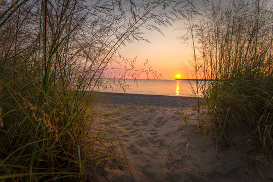 Scenic Sunrise Beach. Summer sunrise framed by dune grass and sandy beach path to the clear waters of Lake Huron. Port Huron, Michigan.