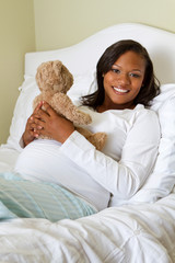 Young pregnant mom holding a teddy bear.