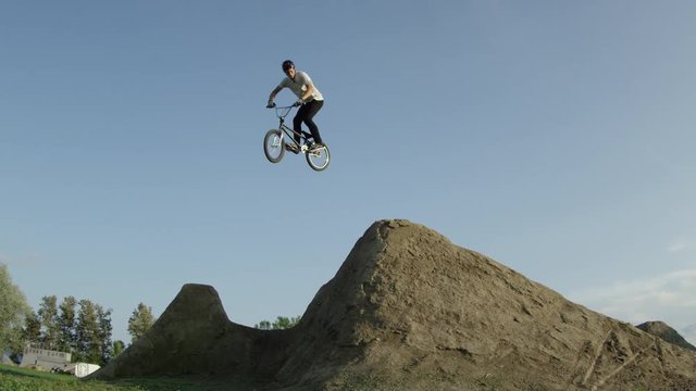Extreme sports athlete doing tricks in slow motion on a big BMX dirt jump with his bicycle