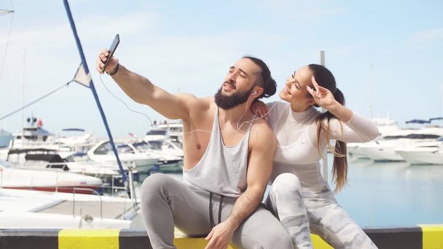Outdoor view of loving young athletic couple in sportswear on summer vacation taking a self portrait with smartphone on seafront
