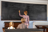Concept of public primary school education with young boy and girl listening to the female teacher