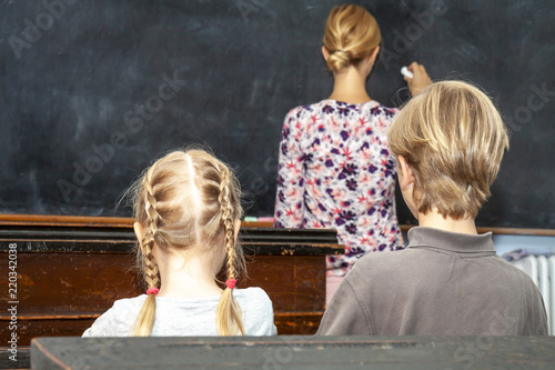 Concept of public primary school education with young boy and girl listening to the female teacher
