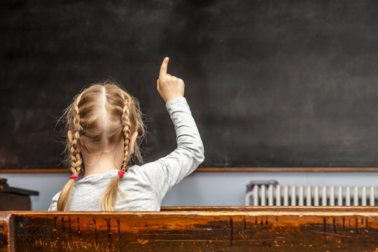 Concept of public primary school education with young girl raising her hand in the classroom