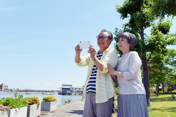 海の近くの公園で、スマホのカメラを構えるシニア夫婦