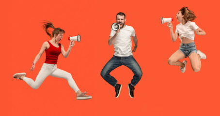 Fototapeta na wymiar Beautiful young man and woman jumping with megaphone isolated over red background. Runnin girl in motion or movement. Human emotions and facial expressions concept
