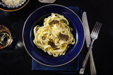 Tagliatelle al tartufo - Italian fresh  pasta with black truffle in blue plate on  wooden rustic...