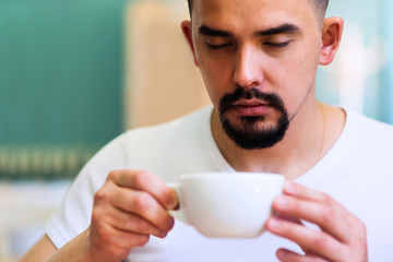 Portrait of a handsome man with beard and moustache meditating with eyses closed over the white coffee mug. Morning coffee ritual