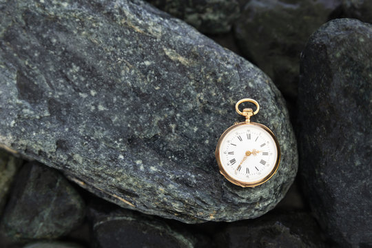 Closeup of a beautiful classic gold pocket watch laying on wet green stones