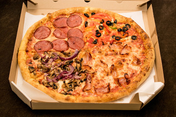 Pizza in a cardboard box on a brown sofa.