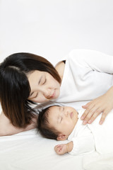 新生児と添い寝しながら赤ちゃんの旨に手を添える若いお母さん、親子の愛と幸せ、母性イメージ