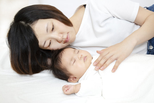 新生児と添い寝しながら赤ちゃんの旨に手を添える若いお母さん、親子の愛と幸せ、母性イメージ