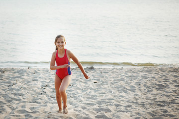 Young pretty girl teenager in a red swimsuit runs along a sandy beach by the sea.