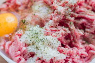 Minced meat in a bowl with raw egg, spices and chopped onion for cooking cutlets, selective focus
