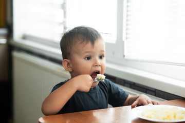 The little boy in the kitchen eagerly eating rice with a spoon independently