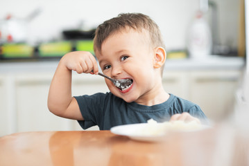 The little boy in the kitchen eagerly eating rice with a spoon independently