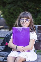portrait of student with notebook and backpack sitting on park bench