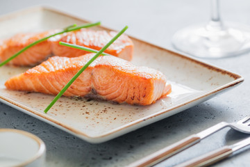The beautiful serving of cooked fried salmon steak on a ceramic plate at a restaurant.
