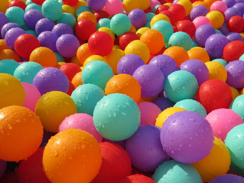 Multi-colored plastic balls in the children's play pool covered with water drops. Wet colorful balls for fun and jumping on kids playground