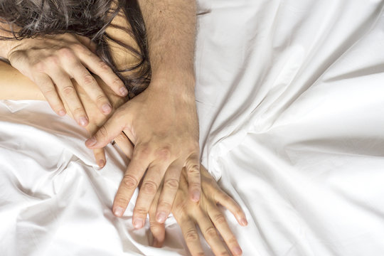 Close up hands of a couple having sex on a bed.