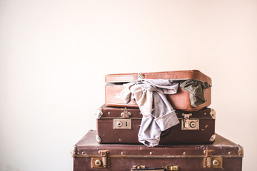 Three old vintage suitcases with clothes on a light wall background. Rustic Retro Style