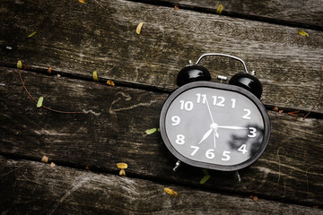Black alarm clock at 7 o'clock on a dark old wooden floor.