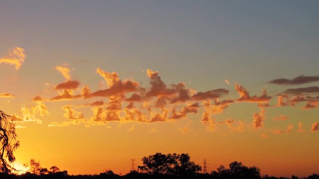 Sunset timelapse of with boiling light cumulus clouds in lurid orange with a natural landscape skyline