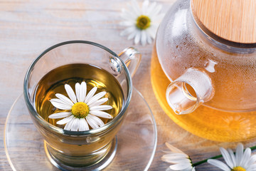 Cup of medicinal chamomile tea and teapot with herbal tea on a wooden background.