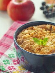 Background with close up of crumble coffee cake served in a bowl. Portion of apple pie decorated with autumn leaves and fresh mint. Vertical. Selective focus on the mint leaf.