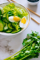 Healthy bowl, cucumber salad with eggs and coriander on marble background