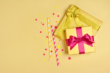 Golden shiny classic gift boxes with pink satin bows and cocktail straws with confetti in the shape of stars as attributes of party