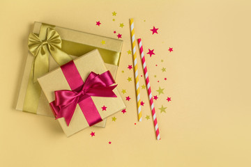 Golden shiny classic gift boxes with pink satin bows and cocktail straws with confetti in the shape of stars as attributes of party