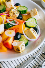 Greek salad of fresh cucumber, tomato, sweet pepper, red onion, feta cheese and olives with olive oil on marble.