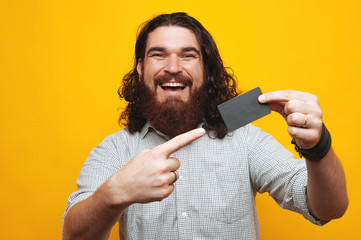 Happy young beard man with long curly hair pointing at credit card