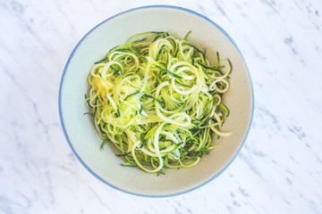 Zucchini spaghetti or noodles (zoodles) in a bowl with marble background Top view overhead