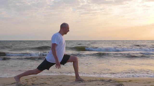 Sportive man stretching leg on seashore with waves at sunrise