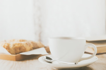 Close up of white coffee cup with croissant on wooden table with vintage tone