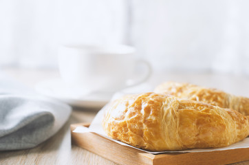 Close up of croissant with cup of coffee on wooden table with vintage tone