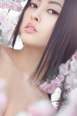 Obraz na płótnie Canvas Outdoor fashion photo of beautiful young asian woman surrounded by flowers on spring. Perfect model with creative vivid makeup and pink lipstick on lips and traditional japanese hairstyle posing