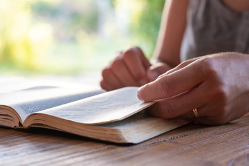 Christian worship and praise. Hands of a young woman on an open Bible in the early morning