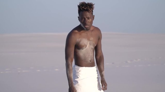 An exhausted black man in a white loincloth is suffering from thirst in the desert, slow motion