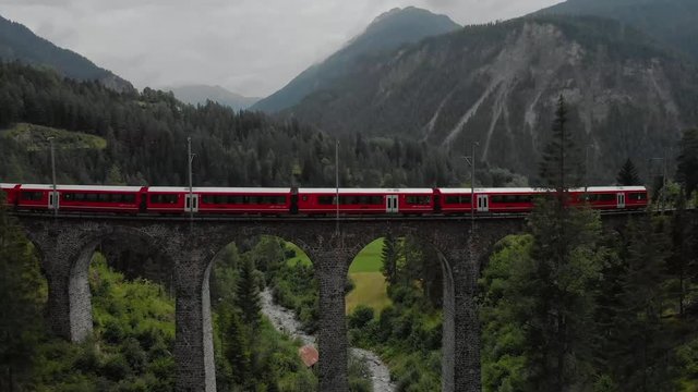 Aerial shot of a train traveling through the Alps on a viaduct in Switzerland