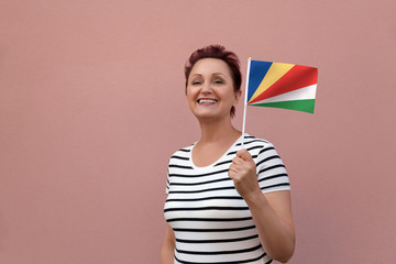 Seychelles flag. Woman holding Seychelles flag. Nice portrait of middle aged lady 40 50 years old with a national flag over pink wall background outdoors.