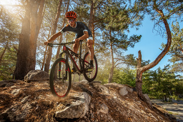 Cross-Country biker on forest trail. Male cyclist rides the rock