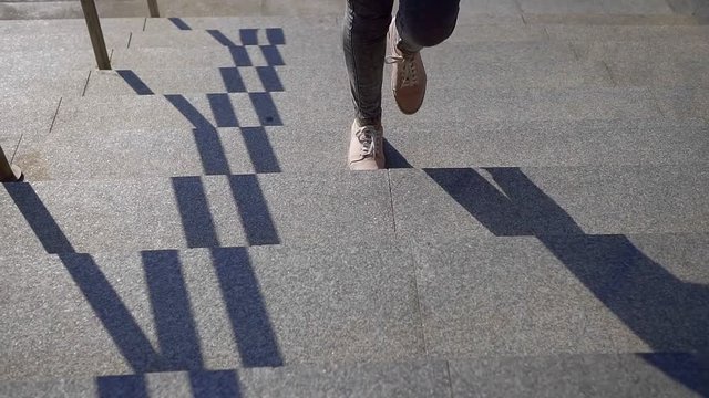 Close-up of woman legs in pink shoes and jeans climb the stone stairs up on a Sunny day