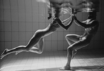 monochrome underwater portrait of the sporty dancing and doing yoga asanas couple underwater in the...
