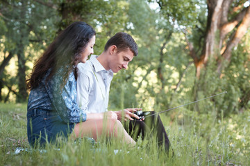 Fototapeta premium young couple sitting on the grass in the forest and looking on sunset, listen to radio, summer nature, bright sunlight, shadows and green leaves, romantic feelings