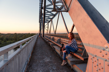 teen girl wanderer sitting on steel bridge design in docks and looking away at sunset